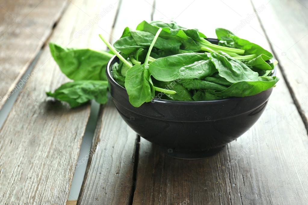 Fresh spinach in a wooden bowl on a wooden table