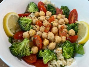 bowl filled with tomatoes, broccoli, chickpeas, rice, and garnished with lemon