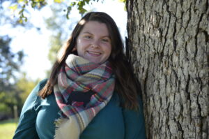 young woman wearing a scarf standing against a tree