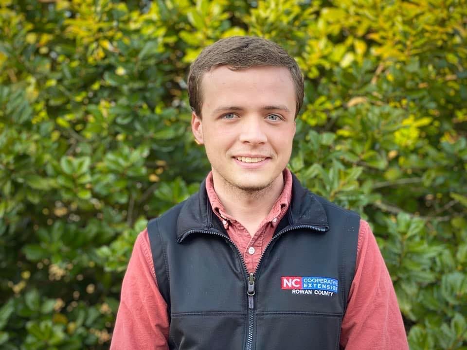 young man smiling in red shirt and black vest