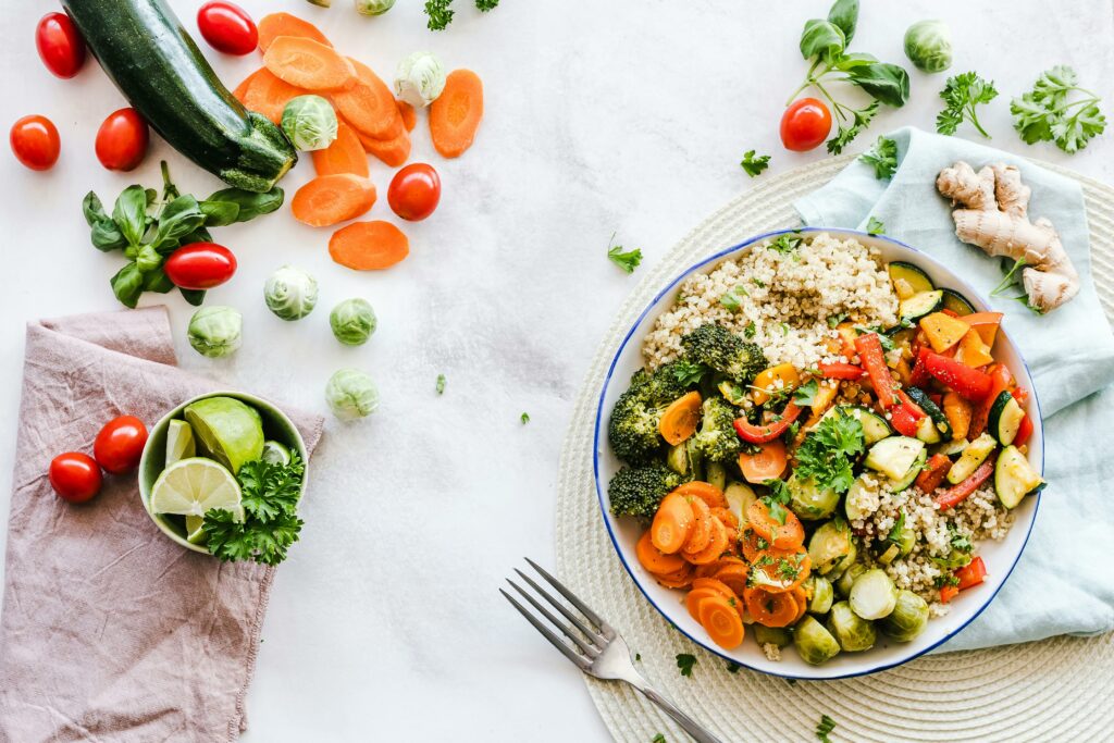 bowl of quinoa and vegetables on table with vegetables scattered around it