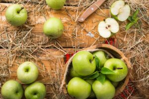 several green apples lying on a wooden table covered in straw