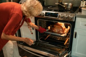 person bent over removing cooked turkey from an open oven