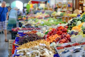 close up of various fruits and vegetables in bins at a farmers market. People walking in the background.
